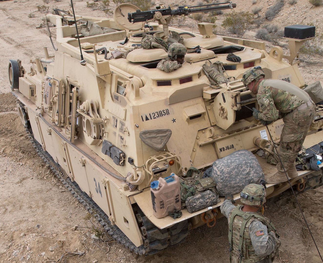 Army soldiers working on a large tan track wheeled vehicle in the desert.