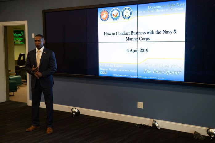 Carlton Hagans stands in front of a Powerpoint presentation for conducting business with the Navy and Marine Corps.