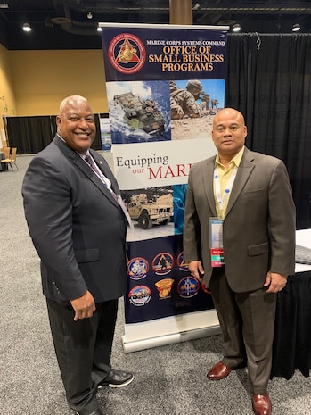 AJ Johnson and Rob Myles pose next to a sign for Office of Small Business Programs.