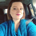 Woman in blue sweater sitting in car, wearing seat belt.