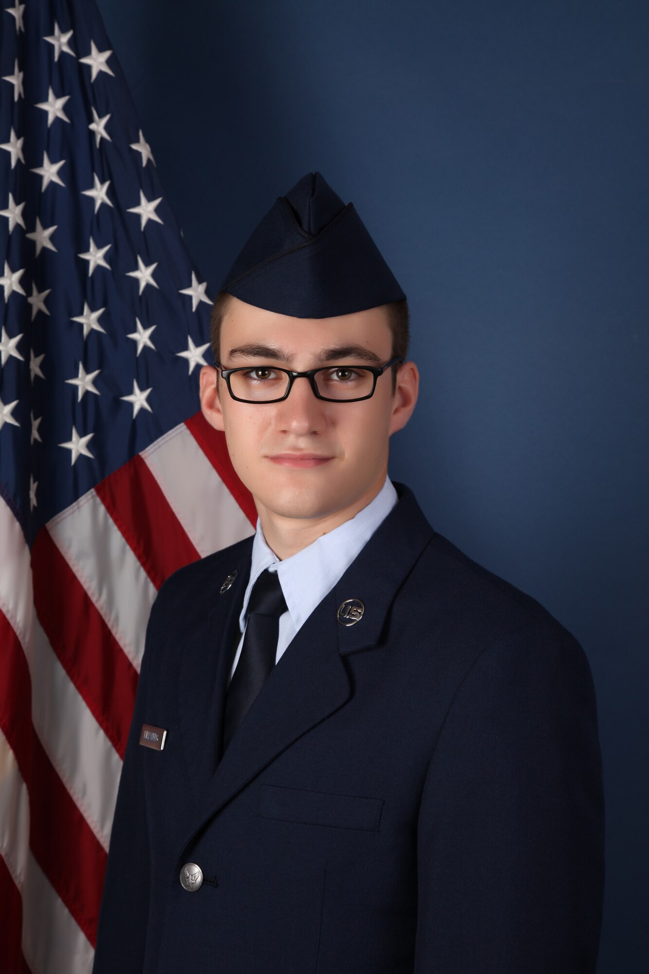 An Airman in dress blues poses for a portrait in front on an American flag.