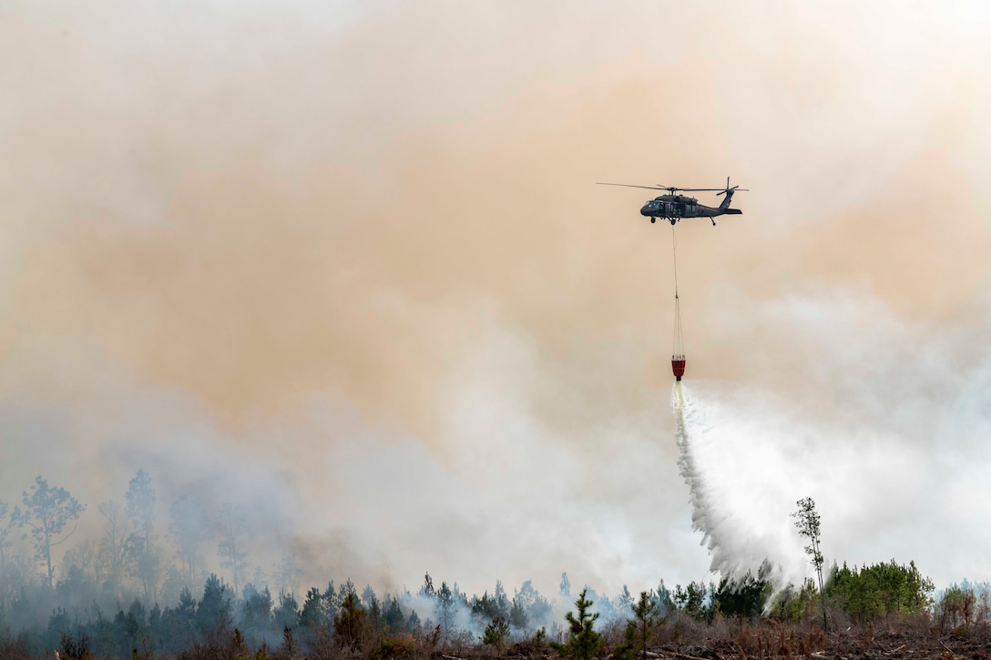 A helicopter uses a bucket to pour water onto a wildfire.