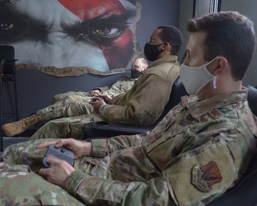 Three men in uniform relax in lounge chairs with video game controllers in their hands.