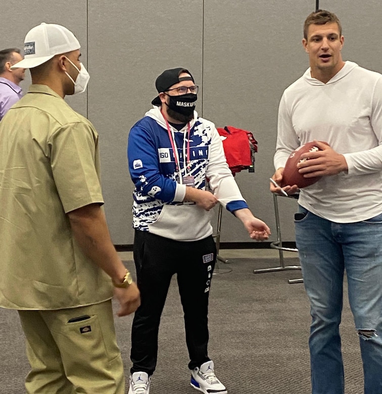 Three men stand near each other in a room. One holds a football.