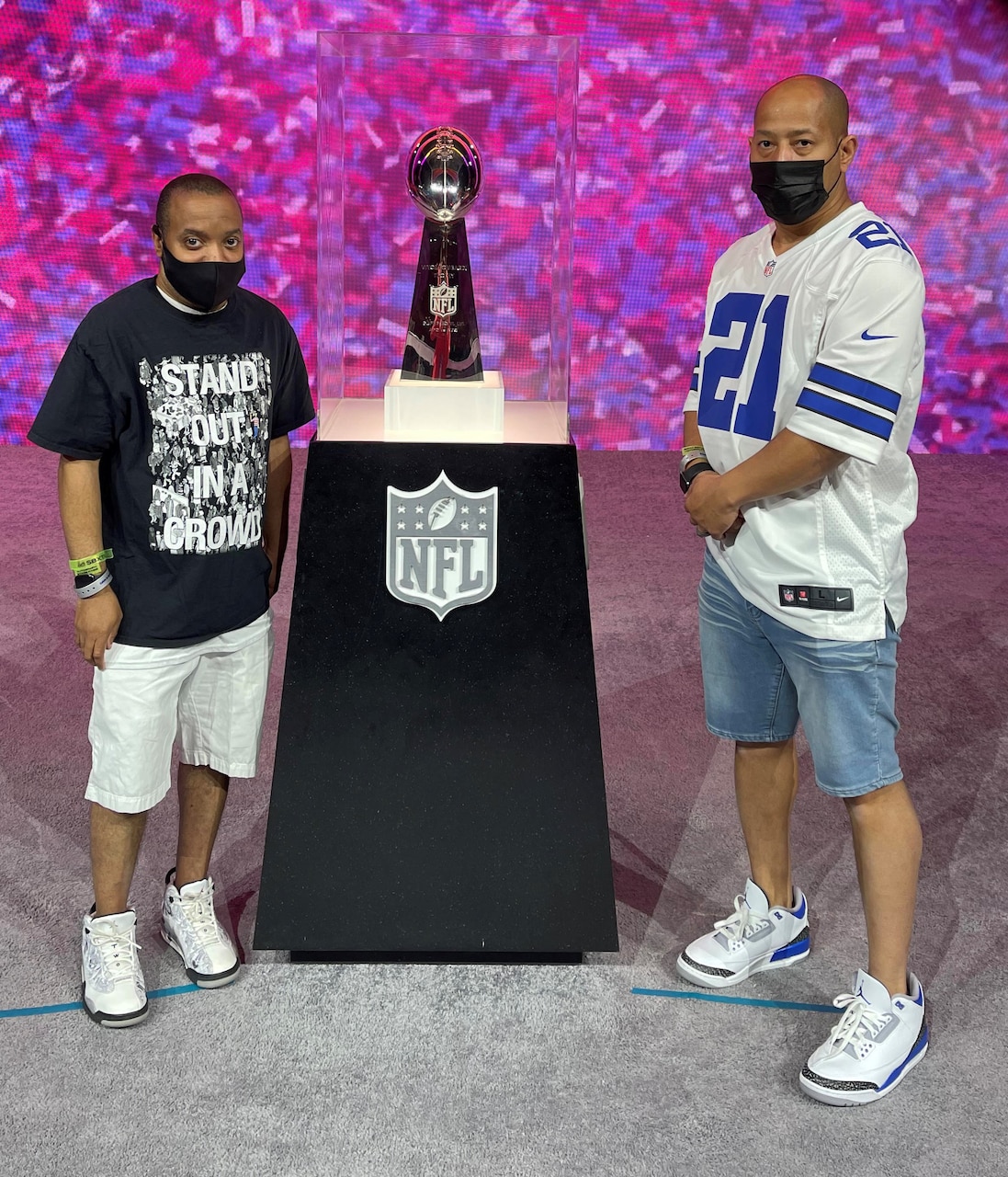 Two men stand in front of a glass-encased trophy on a podium.