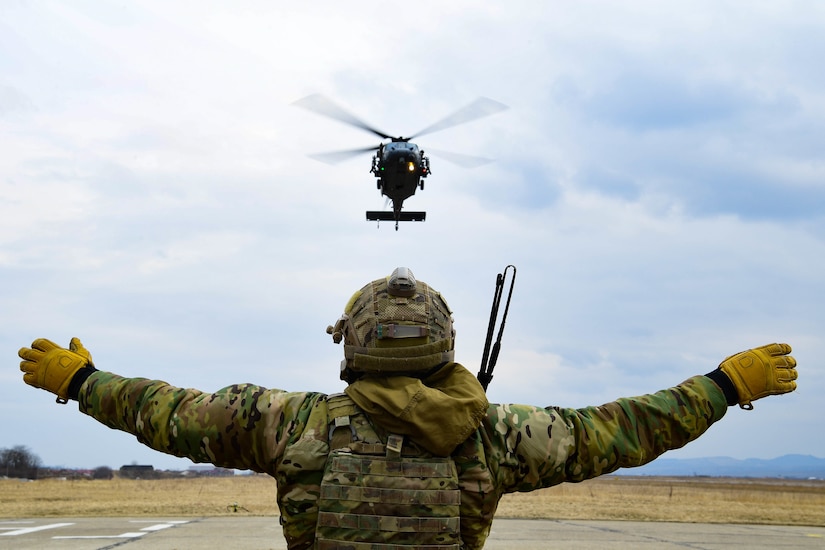 A service member on ground directs a helicopter.
