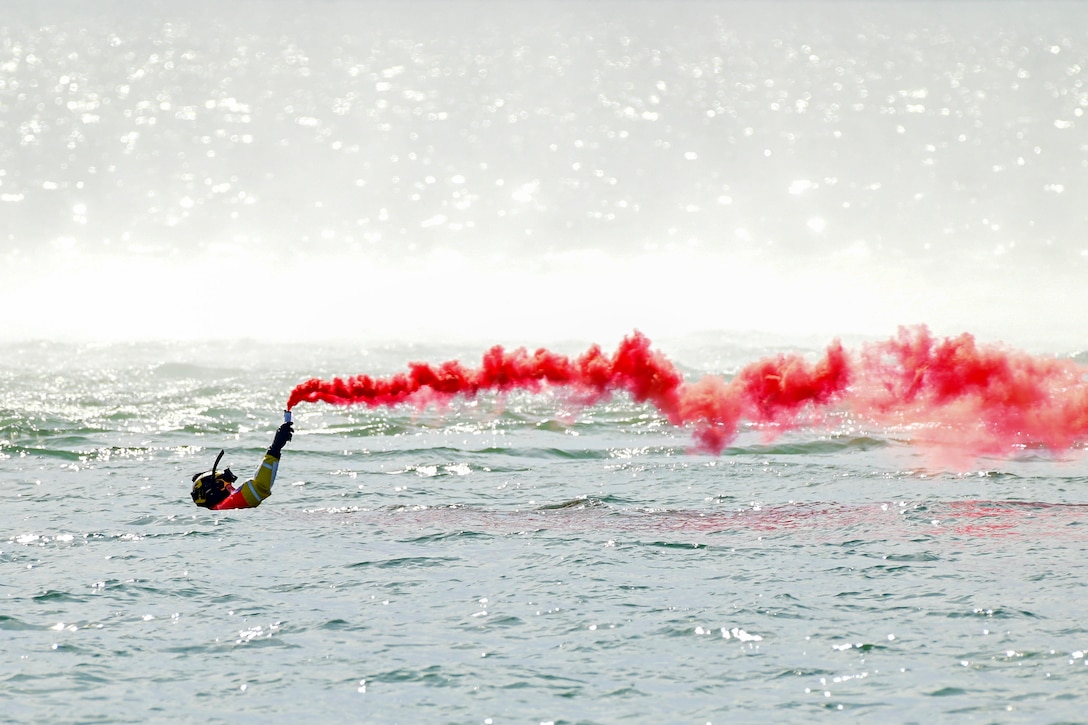 A Coast Guardsman floating in the water uses a red signal flare.