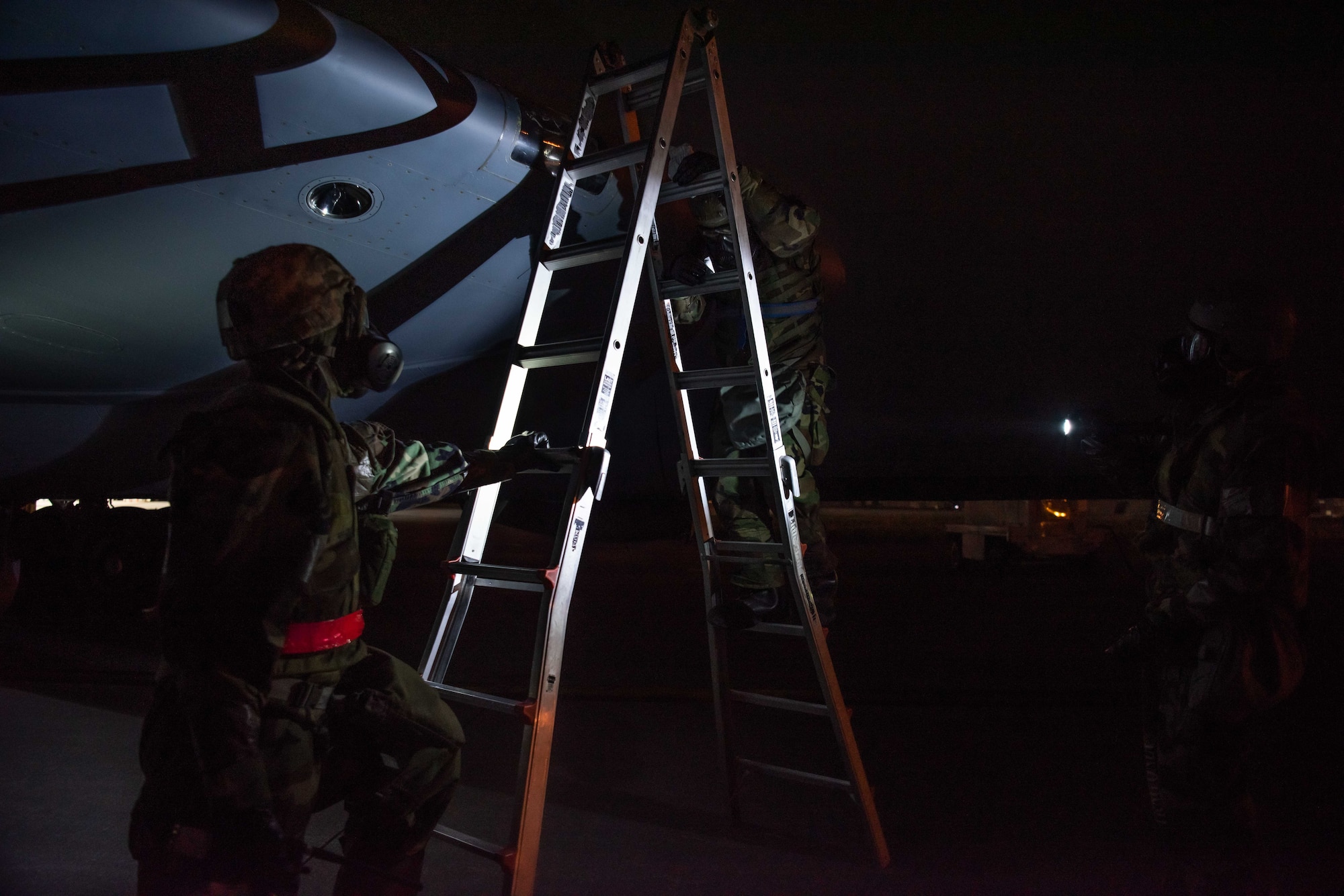 Airmen in protective gear work together to use a ladder to inspect the wing of a KC-135 Stratotanker.