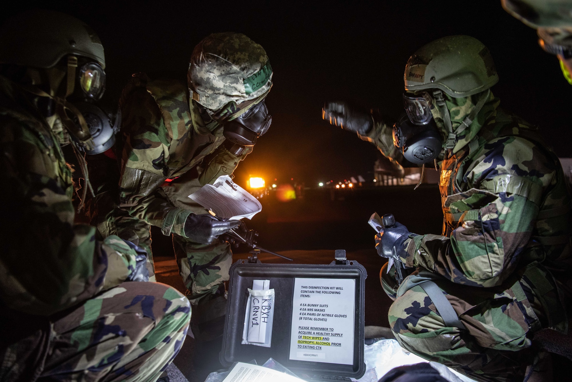 Three Airmen in protective gear go over a decontamination checklist.