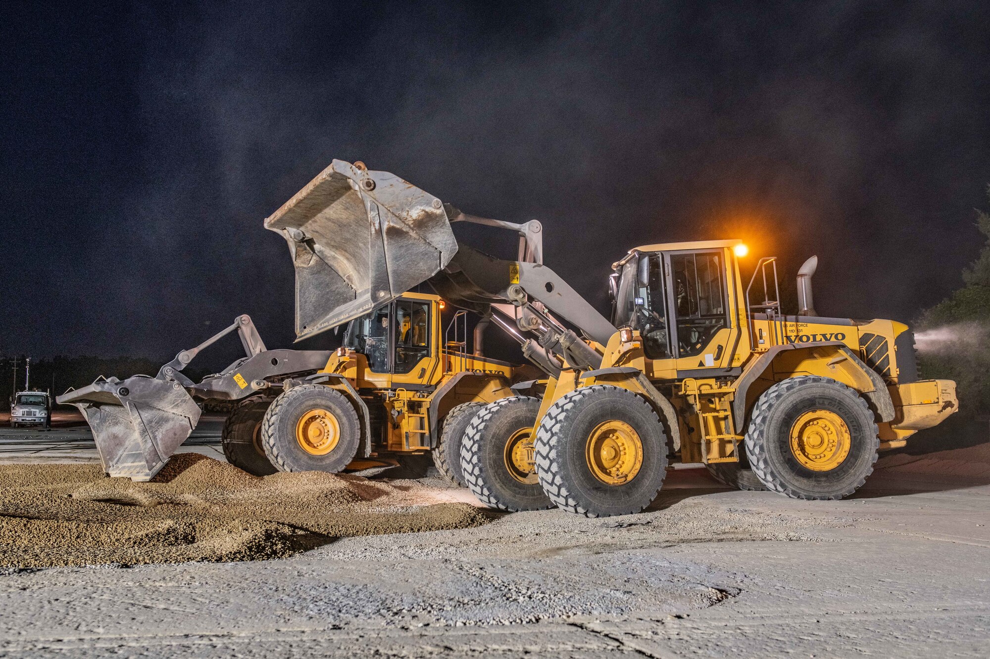Two yellow tractors flatten and dump gravel in a hole.