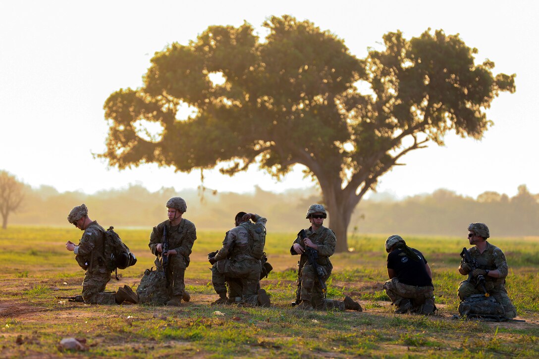 Six soldiers kneel on the ground and work with their equipment.