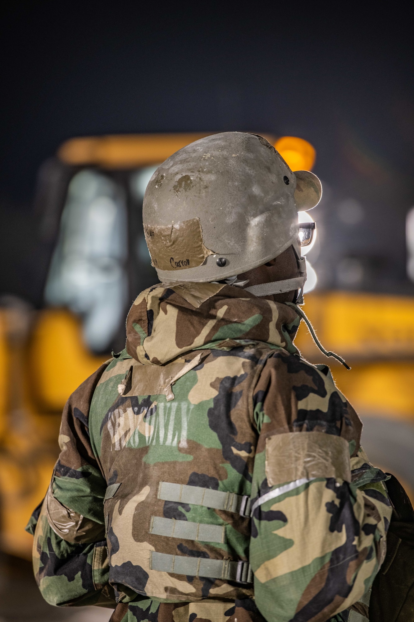 An Airman is blasted by light as a yellow tractor moves in the background