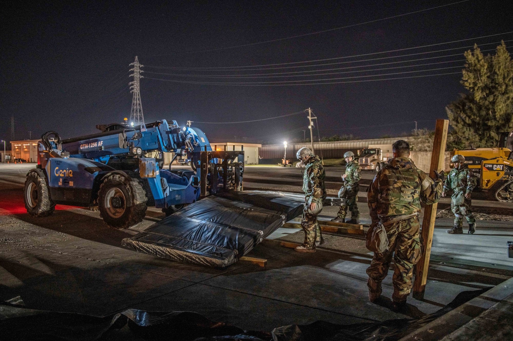 A forklift waits with a package of metal sheets while airmen set down pylons