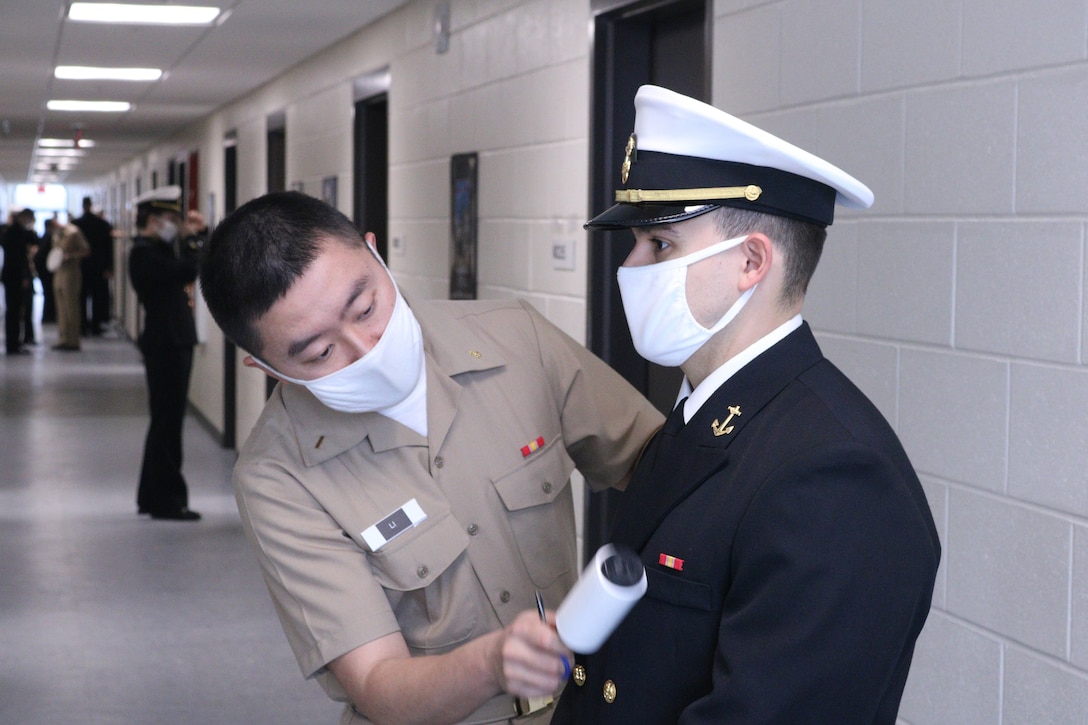 A sailor brushes lint from another sailor's uniform.