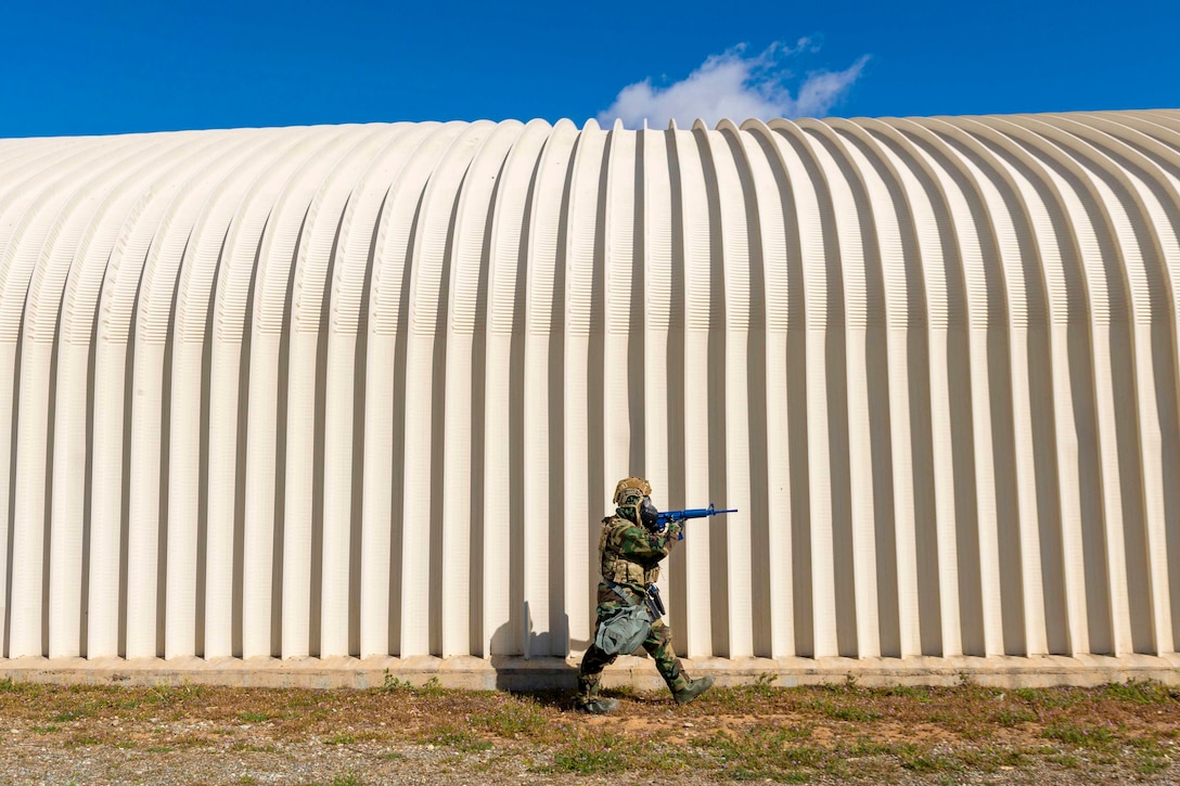 An airman walks next to a building while holding a weapon.