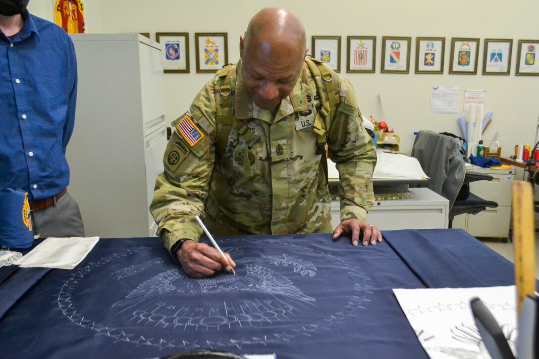 Sgt. Maj. Jimmy Sellers, Army Headquarters G-4 Deputy Chief of Staff signs his name onto a tracing of a presidential flag in production while touring the flag room during his visit to DLA Troop Support March 9, 2022. During his visit, Sellers met with members of all four supply chains, as well as the Troop Support commander and his staff, to get a better understanding of the organization’s mission.