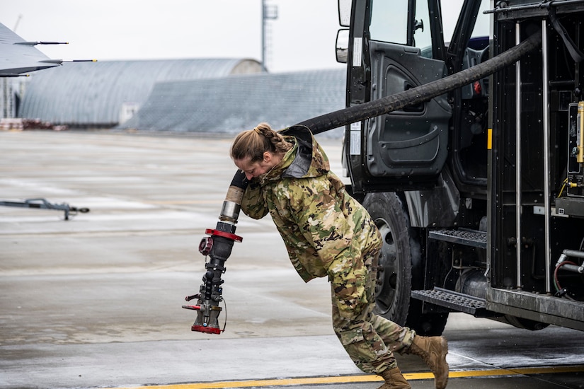 An airman hauls a fuel hose.