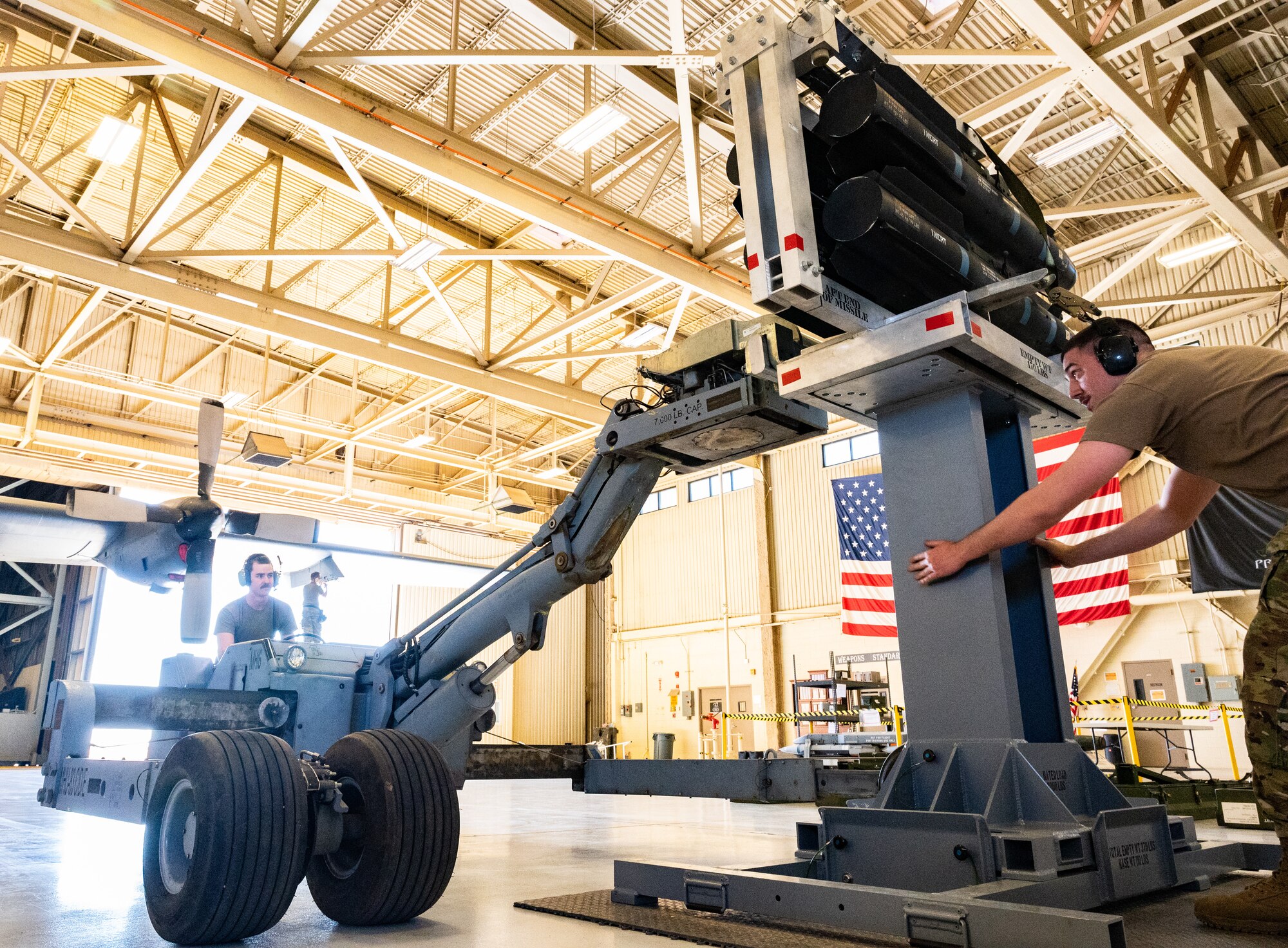 An Air Force sergeant steadies a platform while another Airman uses a bomb lift truck to lower a rack of missiles onto the platform.