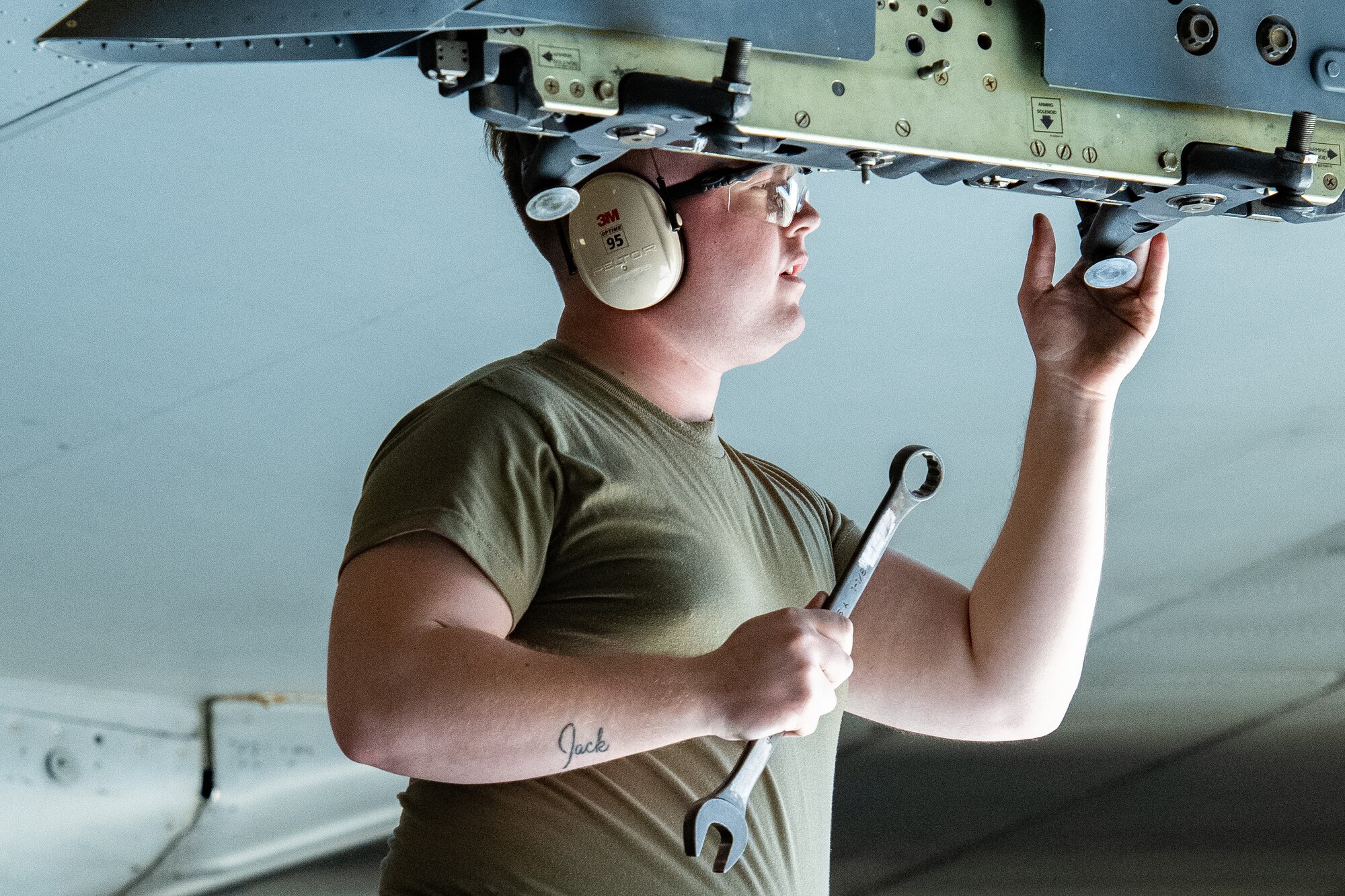 An Airman holding a wrench works the wing of an aircraft.