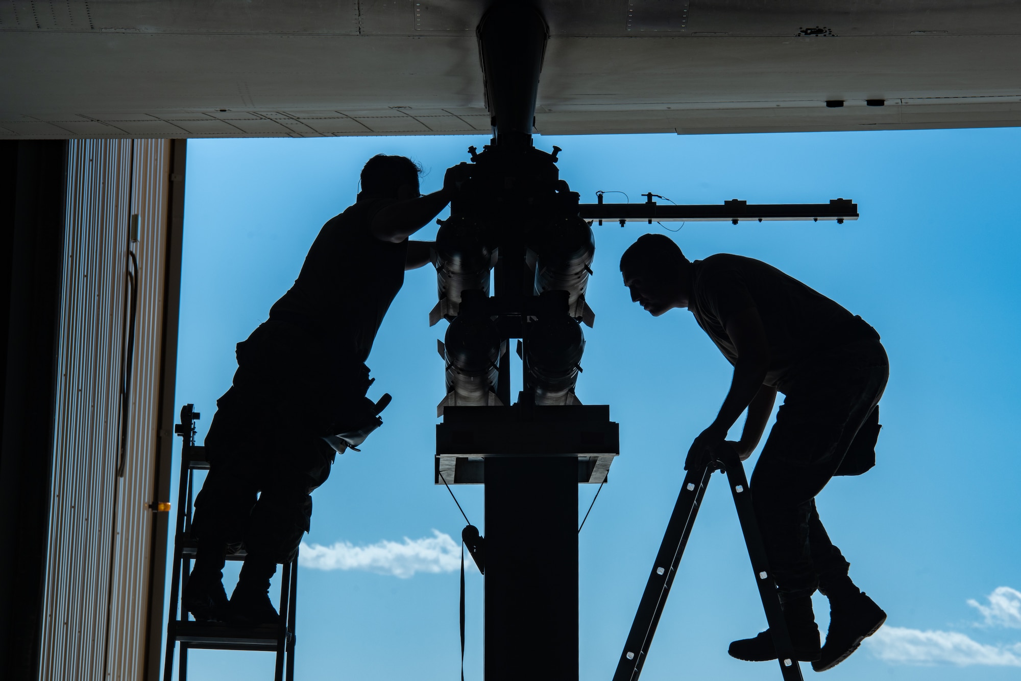 An Airman on a ladder works on missiles attached to the wing of an aircraft while an Airman on the other side of the missiles climbs down a ladder.