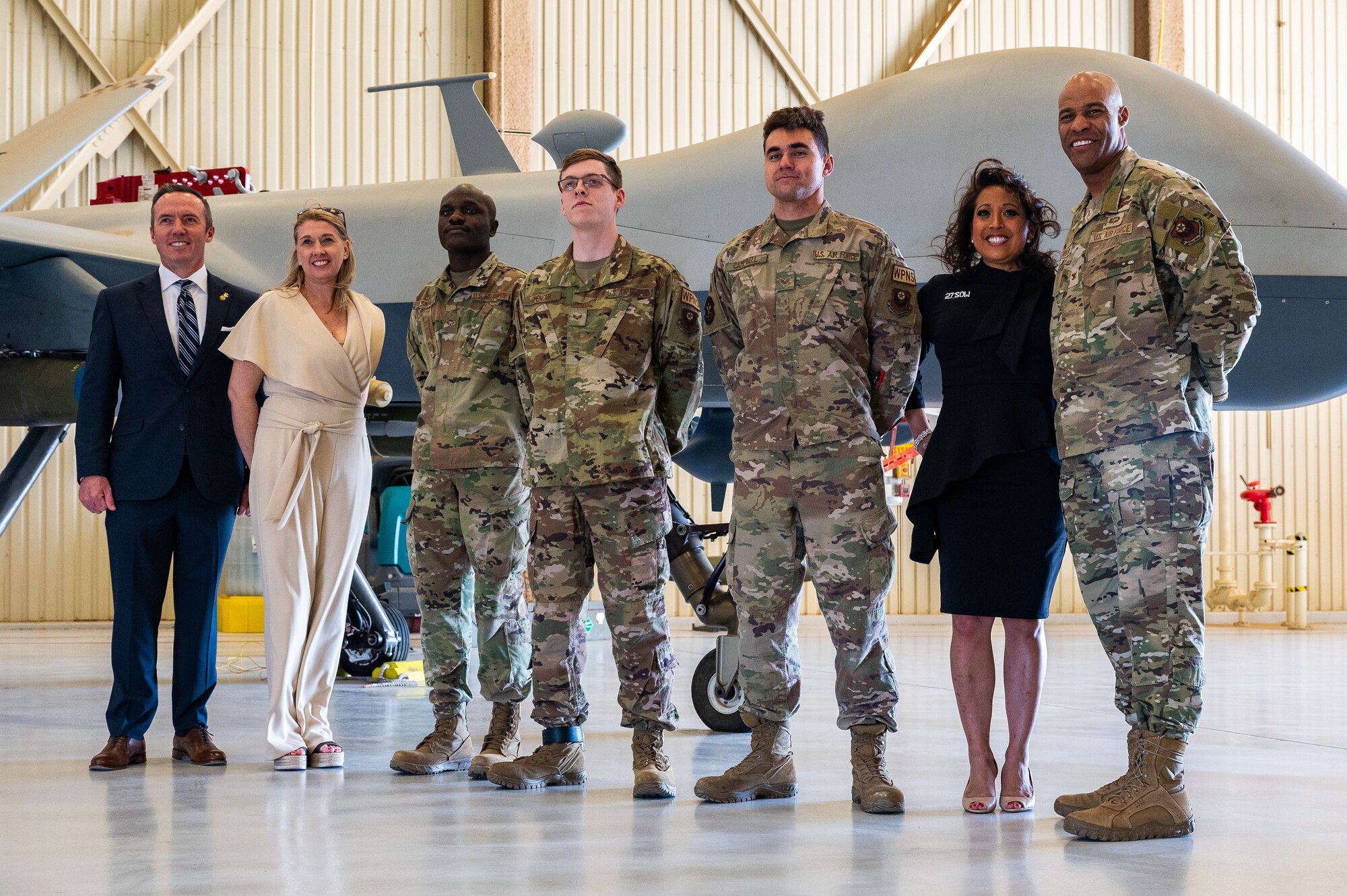 A group of Airmen, a man in a business suit and two women in business attire pose for a group photo in front of a remotely piloted aircraft.