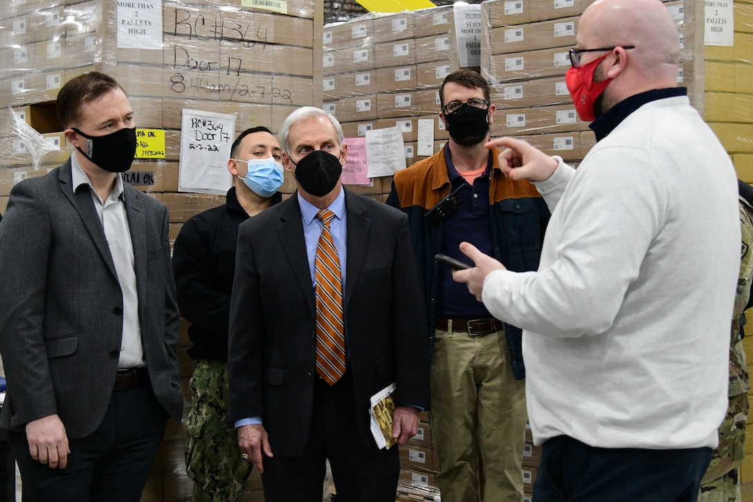 Five people hold a meeting near pallets of COVID-19 test kits.