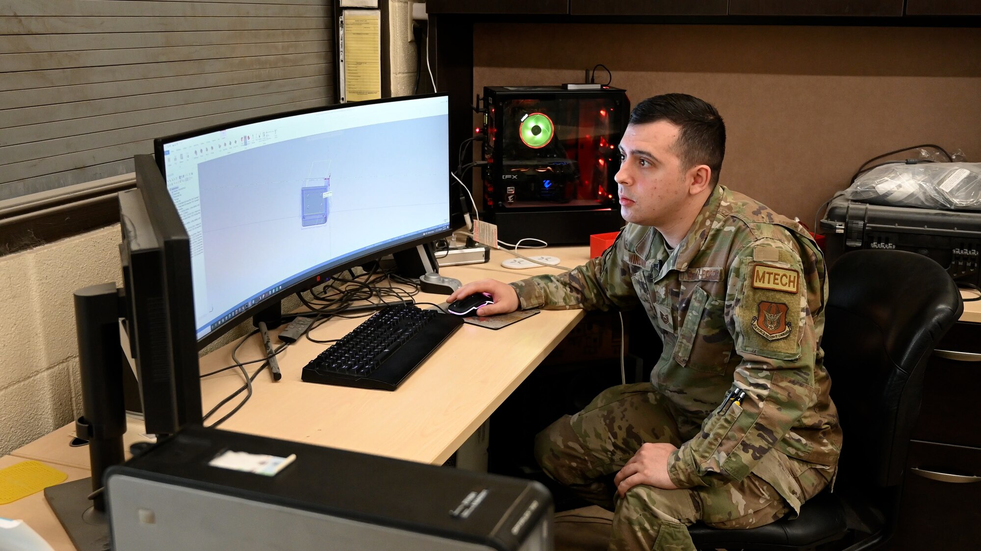 Man in uniform sitting at a desk looking at a computer screen.