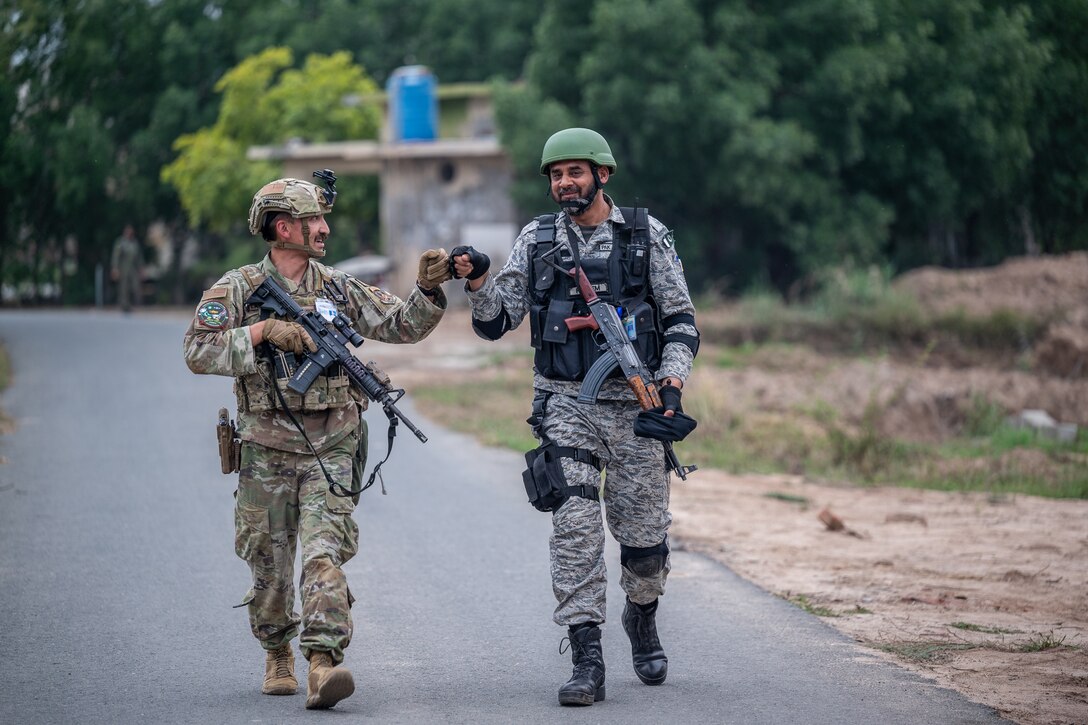 An airman and a Pakistani airman fist-bump while walking on a road.