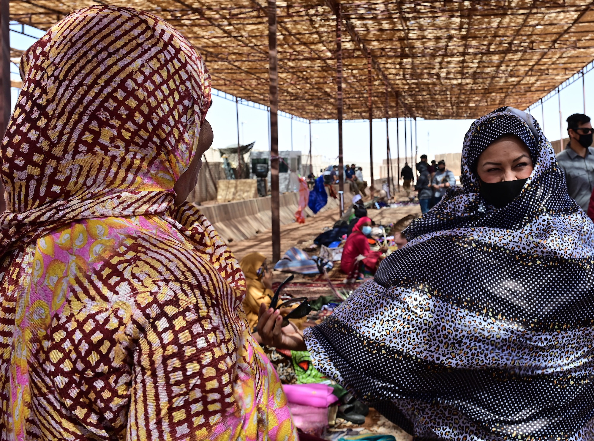 U.S. Air Force Maj. Maribel Seegmiller (right), 724th Expeditionary Air Base Squadron director of operations, tries on a traditional African dress during a bazaar at Nigerien Air Base 201, Agadez, Niger, Feb. 27, 2022.  Over 40 local vendors from the city of Agadez and surrounding villages attended the bazaar, selling various goods. U.S. service members purchased approximately 10,532,000 West African CFA francs ($18K USD) worth of merchandise. Events like these enhance U.S., Niger relationships and stimulate local economic development. (U.S. Air Force photo by Tech. Sgt. Stephanie Longoria)