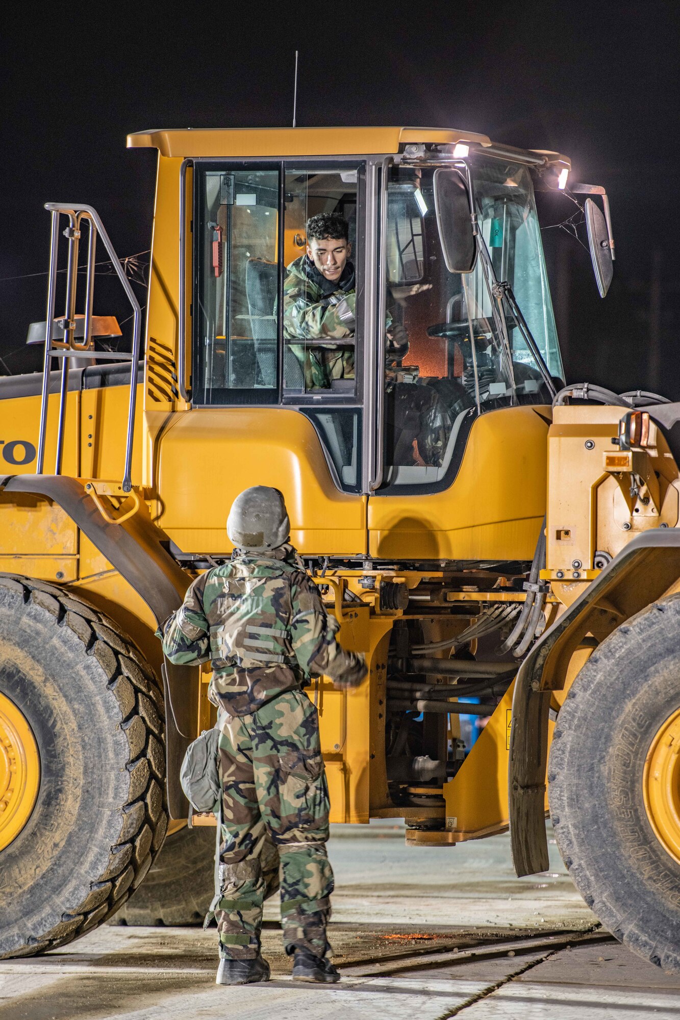 Two Airmen from outside a tractor communicate with one another at night