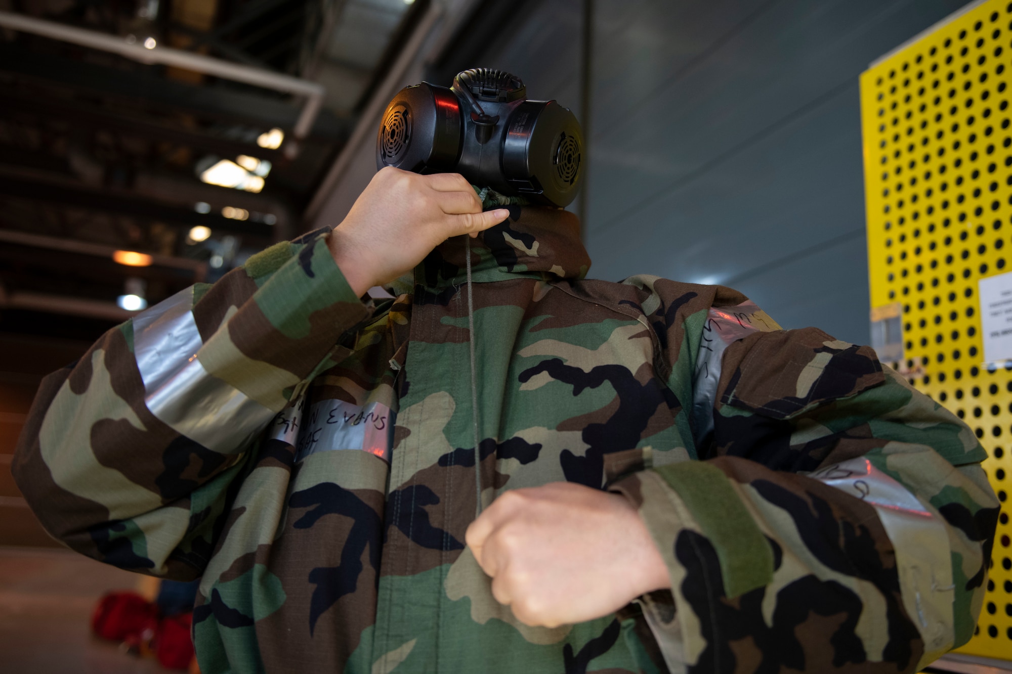 A U.S. Air Force Airman fastens his mission-oriented protective posture (MOPP) jacket hood over his gas mask to ensure a proper seal during a chemical, biological, radiological and nuclear (CBRN) defense survival skills training course at RAF Alconbury, England, March 8, 2022. Airmen are refreshed on vital skills that may save their lives while on duty by learning proper ways to put on protective equipment in a timely and efficient manner. (U.S. Air Force photo by Senior Airman Jennifer Zima)
