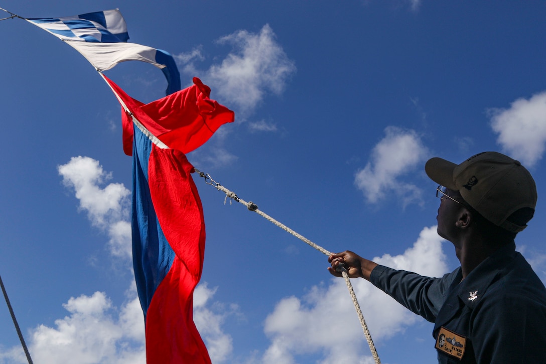 A sailor raises flags against a blue sky.