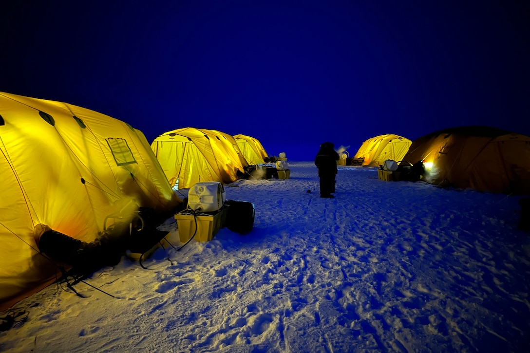 Large tents sitting on snow and ice are illuminated at night.