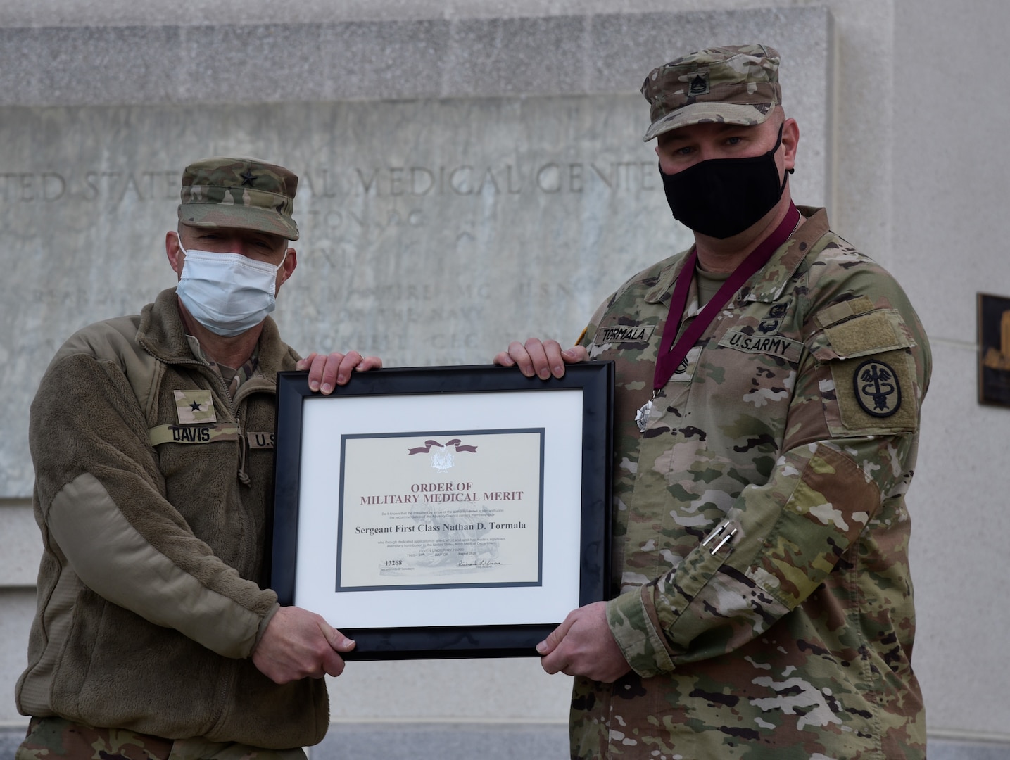 Walter Reed National Military Medical Center's Director Army Brig. Gen. Jack Davis, left, presents an Order of Military Medical Merit certificate to Army Sgt. 1st Class Nathan Tormala outside of WRNMMC, March 10, 2022