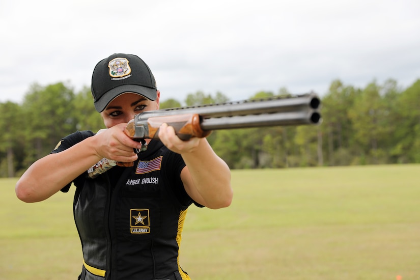 Woman holds a shotgun in the firing position and looks down its sights.