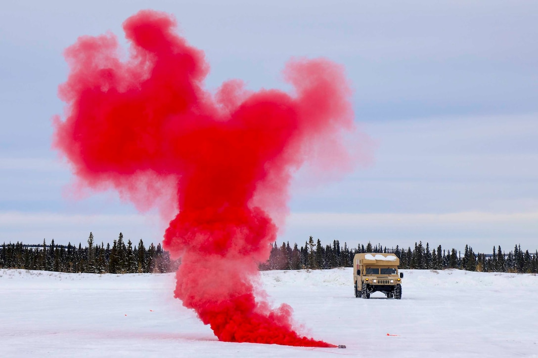 Red smoke rises from a snowy ground as a military vehicle drives in the background.