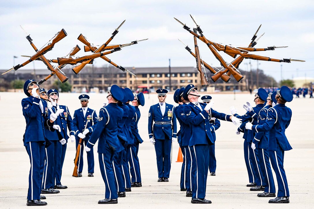 Airmen twirl rifles in the air.