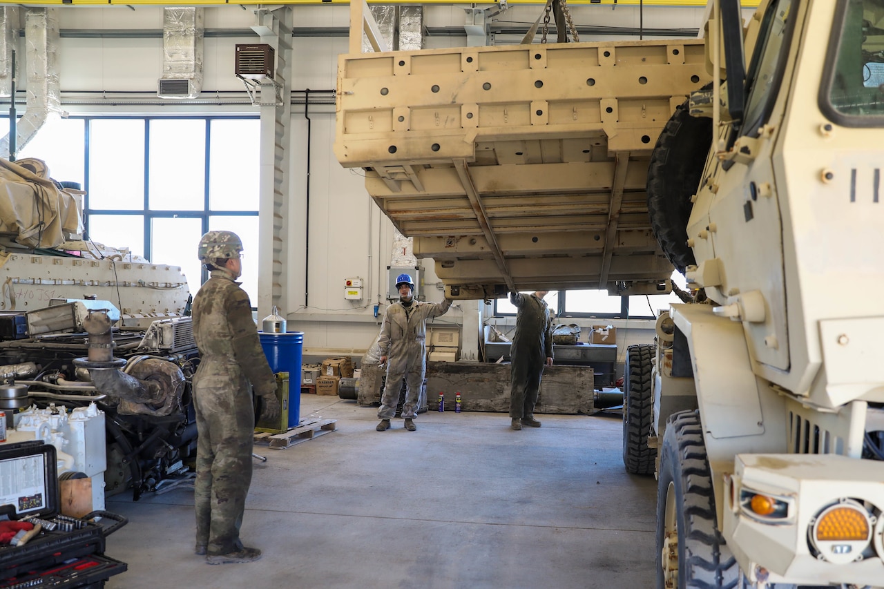 Three workers watch as the bed of a truck is hoisted in the air.