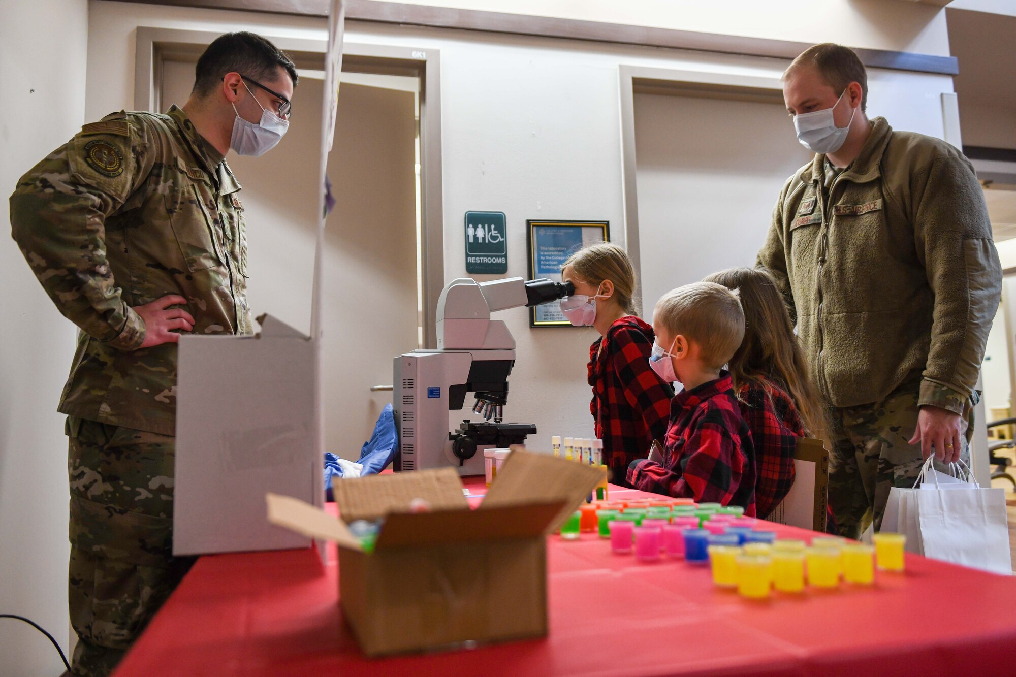 Airman 1st Class Jesus Franco, 22nd Health Care Operations Squadron medical laboratory technician, guides a family through the operation of a microscope during Bring Your Kid to Work Day March 11, 2022, at McConnell Air Force Base, Kansas. The day celebrated the different jobs military parents have, and allowed their children and grandchildren the chance to operate some of the equipment Airmen use every day. (U.S. photo by Staff Sgt. Adam Goodly)