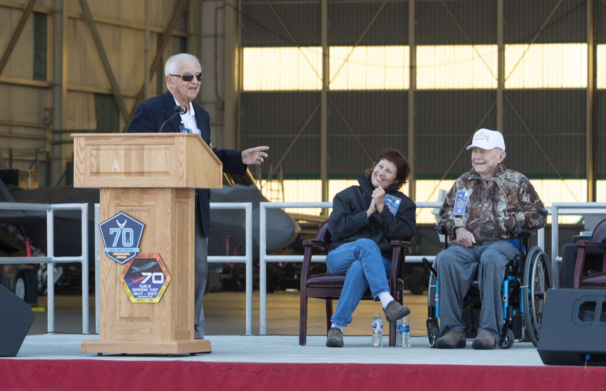 Retired Brig. Gen. Robert Cardenas speaks at the opening ceremony of the 70th Anniversary of Supersonic Flight held Oct. 13 on Ramp 6. Behind him is retired Brig. Gen. Chuck Yeager and wife Victoria. Cardenas piloted the B-29 launch aircraft that released the X-1 experimental rocket plane in which Yeager, a captain at the time, became the first man to fly faster than the speed of sound.