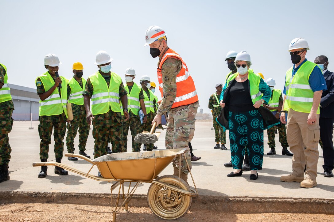 U.S. Army Corps of Engineers North Atlantic Division Commander Brig. Gen. Thomas Tickner shovels a ceremonial scoop of concrete while U.S. Ambassador Mary Beth Leonard, Deputy Director for the Air Force Security Assistance and Cooperation Directorate Ronald Taylor and Nigerian Air Force personnel look on at the site where replacement concrete apron sections will be completed outside of a hangar at Kainji Air Force Base in Nigeria on February 15, 2022. The officials participated in a groundbreaking ceremony highlighting the ongoing construction the U.S. Army Corps of Engineers is managing.  The construction is a part of the historic $500 million U.S. foreign military sale to Nigeria, which also includes the delivery of the 12 A-29 Super Tucano aircraft, munitions, and training. (Photo Courtesy of the U.S. Embassy in Nigeria)