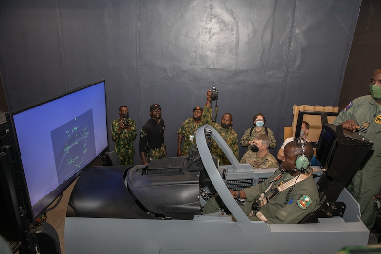 U.S. Army Corps of Engineers North Atlantic Division Commander Brig. Gen. Thomas Tickner, Nigerian Air Force personnel and others look on as a Nigerian Air Force pilot gives a demonstration of flight simulator training at Kainji Air Force Base in Nigeria February 15, 2022. The simulator is housed in a recently constructed temporary facility that will be replaced as part of ongoing construction of additional supporting facilities for the recently delivered A-29 Super Tucano aircraft at the base being managed by the U.S. Army Corps of Engineers. That same day, Tickner and other U.S. officials, including U.S. Ambassador Mary Beth Leonard and Deputy Director for the Air Force Security Assistance and Cooperation Directorate Ronald Taylor, joined Nigerian Air Force officials for a groundbreaking ceremony highlighting the ongoing construction project at the base. The construction is part of a historic $500 million U.S. foreign military sale to Nigeria, which also includes the delivery of the 12 A-29 Super Tucano aircraft, munitions, and training – including the simulator equipment. (Photo Courtesy of the U.S. Embassy in Nigeria)