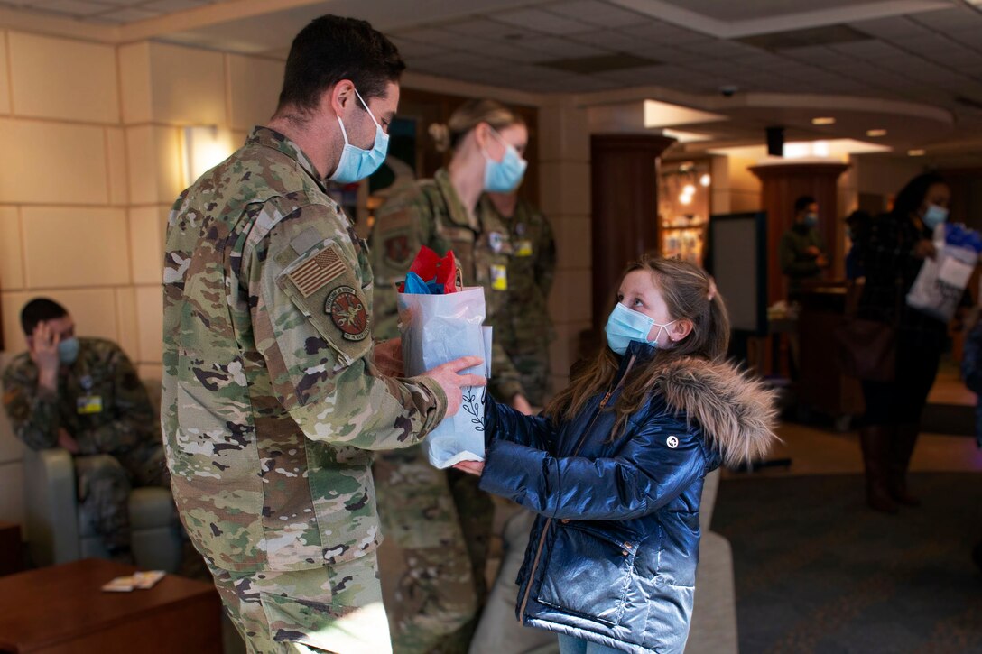 A girl wearing a face mask hands a thank your letter and candy bag to an airman.