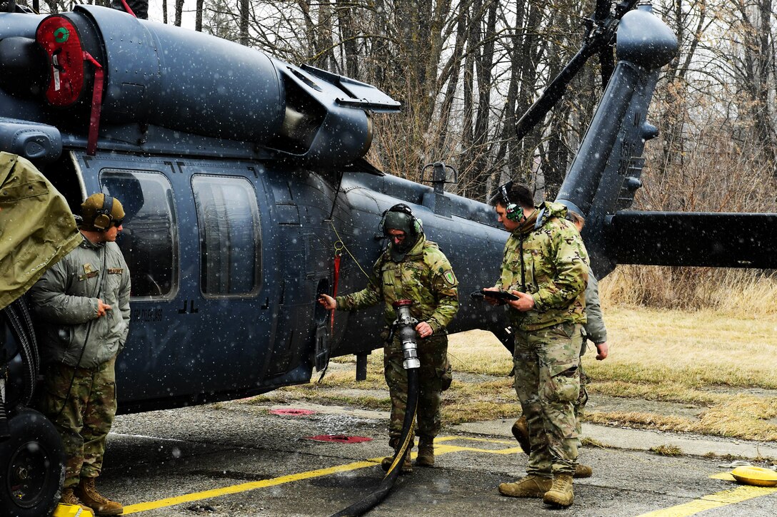 Three soldiers refuel a helicopter.