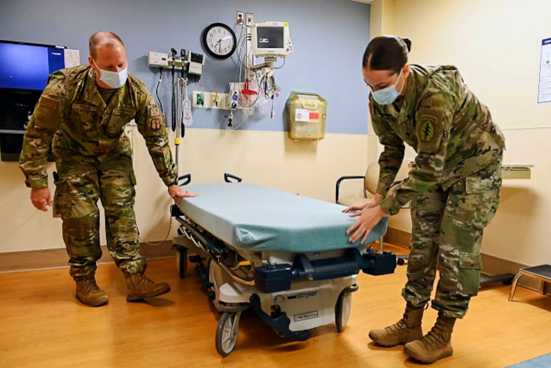 An airman and a soldier wearing face masks prepare a bed.