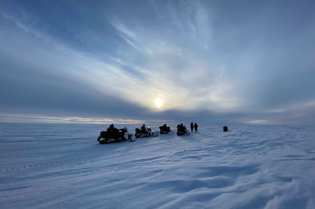 Soldiers on snowmobiles cross snowy tundra at twilight.