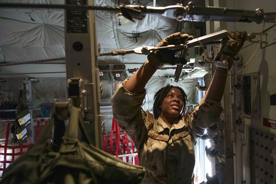 An airman wearing gloves works on cables.