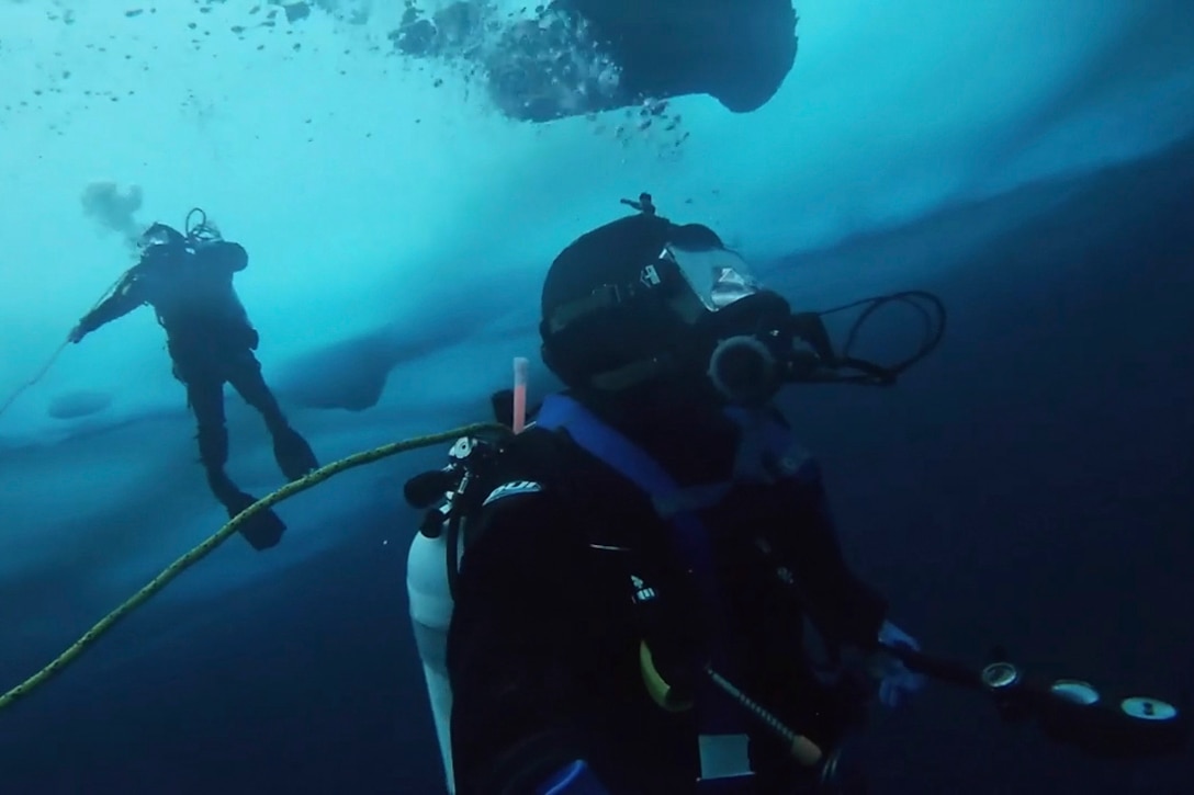 Two sailors swim in a cold body of water.