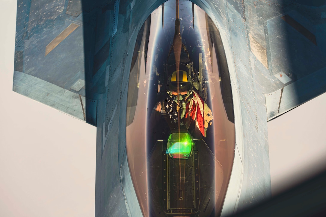 An airman wearing an American flag around his neck flies an aircraft.