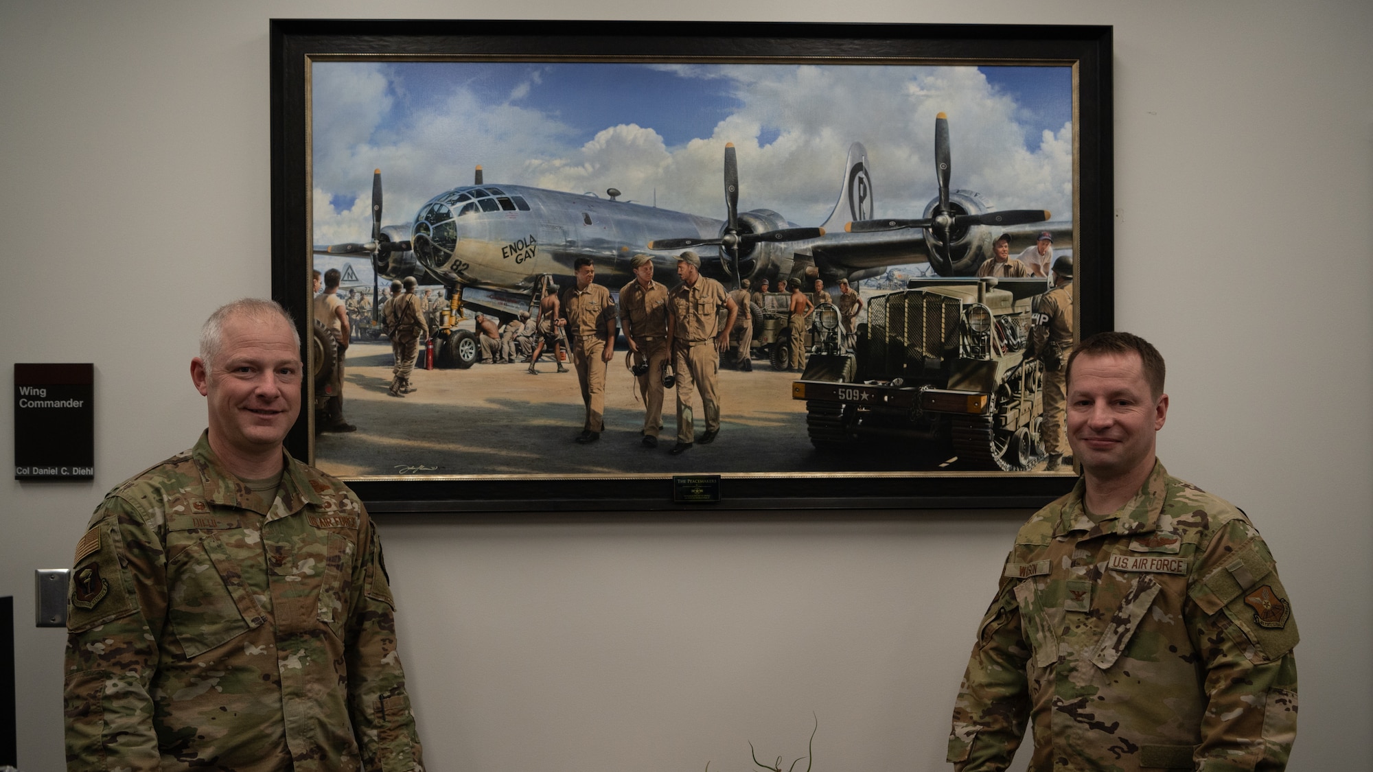 Col. Daniel Diehl and Col. Kyle Wilson stand for a photo next to a painting of the Enola Gay.